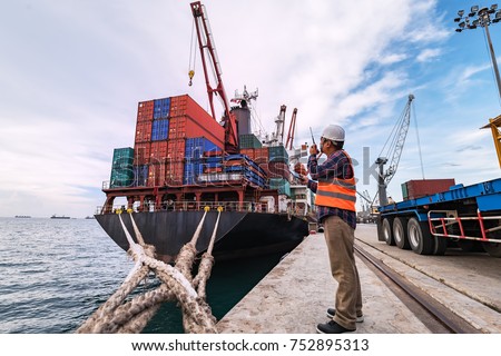 Engineers and crane.smiling dock worker holding radio and ship background