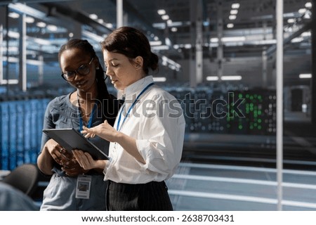 Engineers in data center using device, verifying firewall configurations. Teamworking IT professionals performing equipment vulnerability scans in server hub using tablet