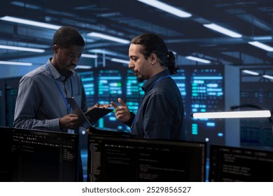 Engineers in data center using tablet and laptop to check for server performance issues arising due to high CPU usage. Server hub workers fixing insufficient memory errors slowing down hardware - Powered by Shutterstock