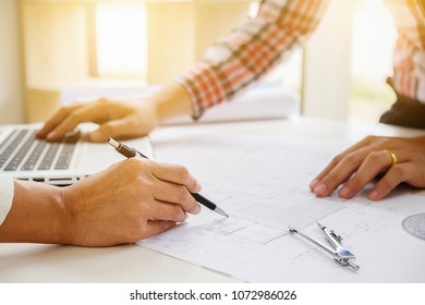 Engineers discuss a blueprint while checking information on a tablet computer in a office.
