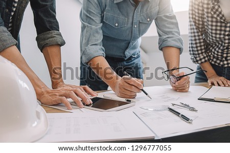 Engineers discuss a blueprint while checking information on a tablet computer in a office.