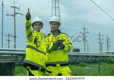 Engineers discuss project details while inspecting power lines in an outdoor setting during overcast weather