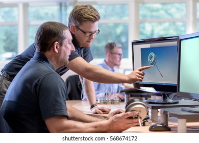 Engineers Discussing  Drawings Onscreen Of Exhaust Valve Actuator In Factory