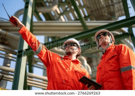 Engineers discussing work using walkie-talkie and tablet at oil and gas plant