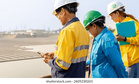 Engineers Examining Data on a Mobile Device at an Industrial Facility by Water During Daytime