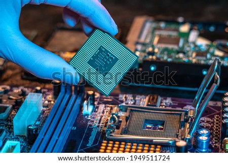 The engineer's gloved hand is holding the CPU chip against the background of the motherboard. Concept of high-tech hardware microelectronics