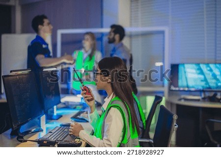 Engineers in high visibility vests collaborate in control room, reviewing digital site plans and dashboards during an operations and safety discussion. Coordination, monitoring, and incident readiness