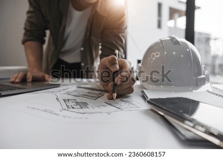Engineers holding a pen pointing to a building and drawing outlay construction plan as guide for builders with details.