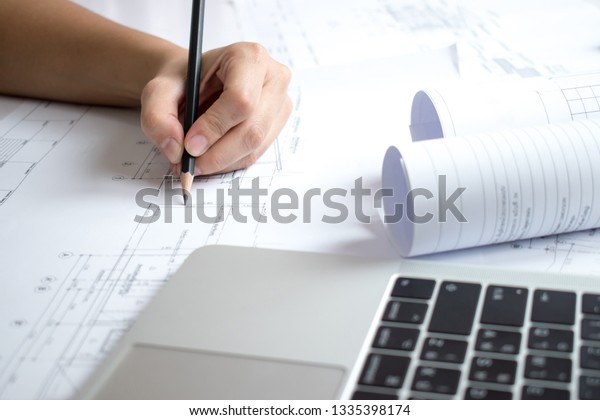 Engineers\
holding a pencil pointing to the blueprint of the house structure\
that is nearing completion, concept\
architect.