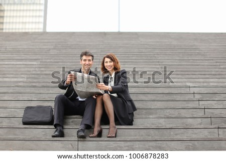 engineers male and female find article about company in newspaper, colleagues sitting on stairs reading. Americans wearing business clothes smiling communicating. Concept of fashionable cl
