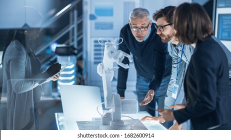 Engineers Meeting in Robotic Research Laboratory: Engineers, Scientists and Developers Gathered Around Illuminated Conference Table, Talking, Using Tablet and Analysing Design of Industrial Robot Arm