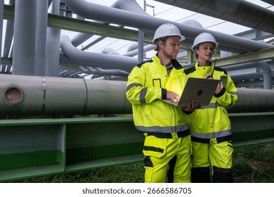Engineers review data while inspecting industrial pipes during daylight hours at a facility