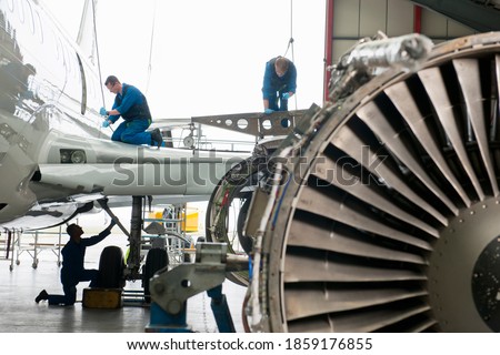 Engineers in safety vests assembling the wing of a passenger jet at a hangar.