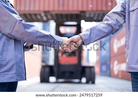 Engineers shaking hands congratulating themselves on success with shipping containers in the background.