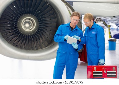 Engineers with a toolbox using a digital tablet next to the engine of a passenger jet at a hangar. - Powered by Shutterstock