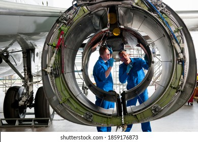 Engineers in uniforms inspecting the engine casing of a passenger jet at a hangar. - Shutterstock ID 1859176873