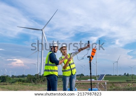 Engineers using meteorological or anemometer instrument collect data laptop to measure the wind speed, temperature,humidity and solar cell system on wind turbine station is sustainable energy concept