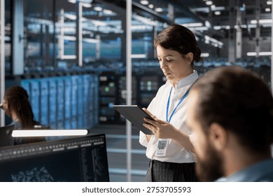 Engineers using tablet in data center, managing server virtualization, running scripts. Woman in server farm using programming language on device to finetune network protocols