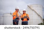 Engineers wearing safety gear, including hard hats examining survey a large blueprint tablet standing industrial facility gas or oil refinery engaged in a job requires high safety standards concept.