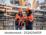 Engineers wearing safety gear, including hard hats examining survey tablet standing industrial facility gas task or oil refinery engaged in a job requires high safety standards concept.