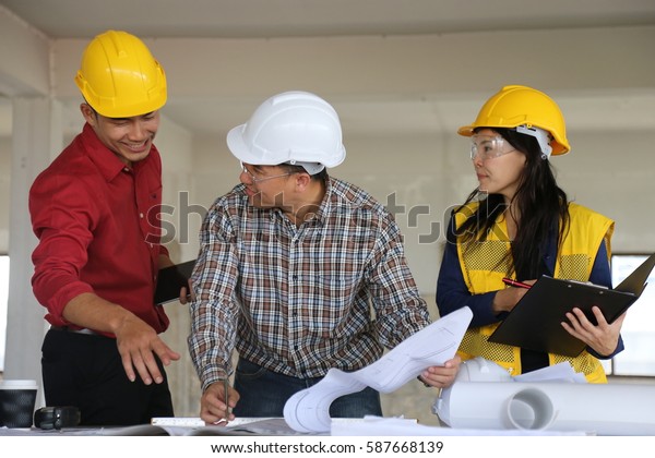 engineers wearing yellow, white helmets\
discussing engineering concepts with engineering tools placed\
before them on the table in their\
workplace