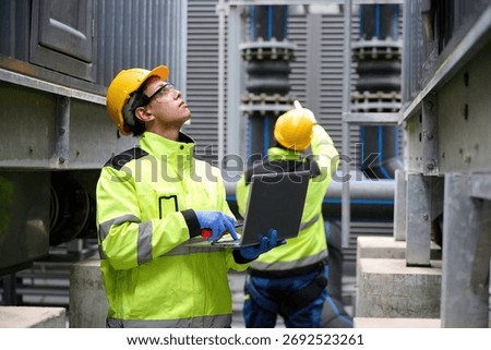 Engineers at work in a technological facility, analyzing with their laptop computer. Focused on the data, the workers are involved in technical operations and maintenance