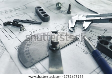 Engineer's workbench with tools, drawings and parts scattered about.