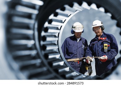 engineers, workers seen through a giant cogwheel and gear axle