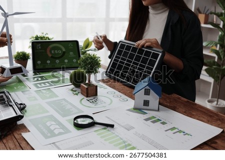 Engineers working with charts and graphs analyzing net zero and ESG project using miniature house, solar panel and wind turbine