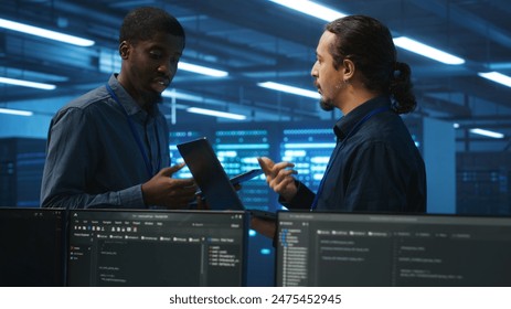 Engineers working in high tech server farm, using laptop and tablet to analyze data, ensuring seamless data flow. Men examining hardware in data center, ensuring system integrity and security