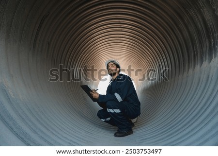 Engineers working inside a large steel pipe of a tunnel foundation. Workers involved in constructing a pipeline for transporting oil, natural gas, and fuel at an industrial factory.