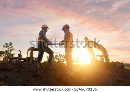 Engineers are working on road construction. engineer holdingradio communication at road construction site with roller compactor working dust road on during sunset