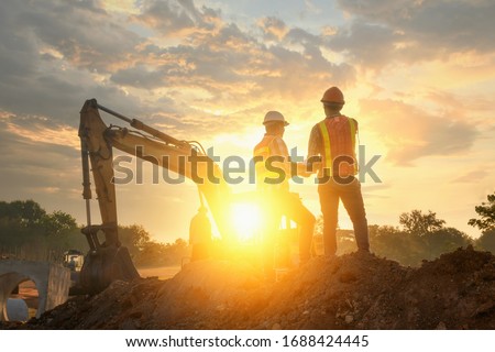 Engineers are working on road construction. engineer holdingradio communication at road construction site with roller compactor working dust road on during sunset