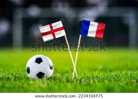England - France. Quarter-finals football match. Round of 8. Handmade national flags and soccer ball on green grass. Football stadium in background. Black edit space.