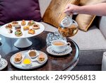 English afternoon tea set including hot tea, pastry, scones, sandwiches and mini pies on marble top table.