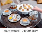 English afternoon tea set including hot tea, pastry, scones, sandwiches and mini pies on marble top table.