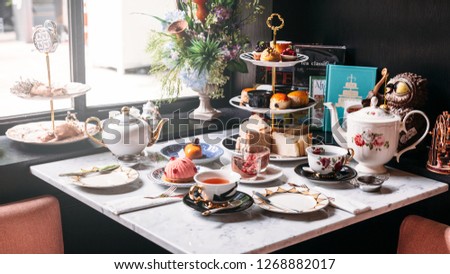 English afternoon tea set including hot tea, pastry, scones, sandwiches and mini pies on marble top table.