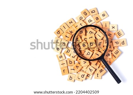 English alphabet made of square wooden tiles with the English alphabet scattered on white background. The concept of thinking development, grammar. Magnifier placed on English letters