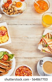 English Breakfast Border On Rustic Wood With Dishes Of Scrambled And Fried Eggs, Mushroom, Tomato, Pork Sausage, Ham Sandwich, Marmalade, Beans, Coffee And Orange Juice