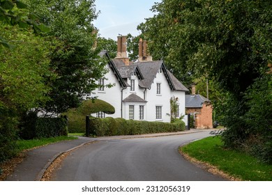 An English country lane in a small village featuring a large whitewashed detached house in a gothic revival style - Shutterstock ID 2312056319
