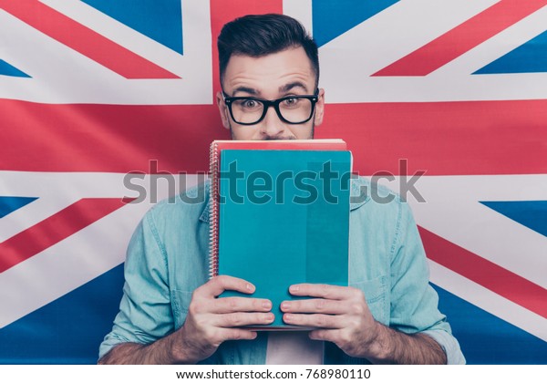 英語学習コンセプト 英語の国旗の背景にノートを掲げ カラフルなコピー本を手で閉じ カラフルな写し本を持つ興奮した男性のポートレート の写真素材 今すぐ編集