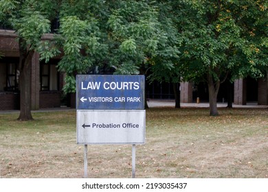 An English Law Courts And Probation Office Sign Board With Trees And Building Blurred In The Background. No People