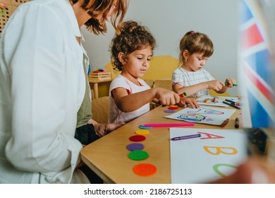 English lesson at elementary school or kindergarten. Students learning alphabet and colors with teacher coloring the letter A sitting in the classroom. Selective focus.