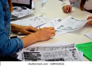 English Lesson In The Exam Room Or In The Classroom, High School. The Teacher Holds A Pencil In His Hand, Checks The Completed Task, Writes Comments.