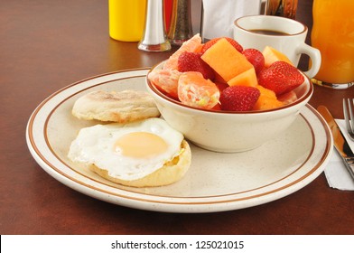 An English Muffin Topped With A Fried Egg And A Bowl Of Fresh Fruit