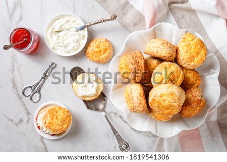English Style Scones with clotted cream and strawberry jam on a white cake stand, horizontal view from above, close-up, flat lay
