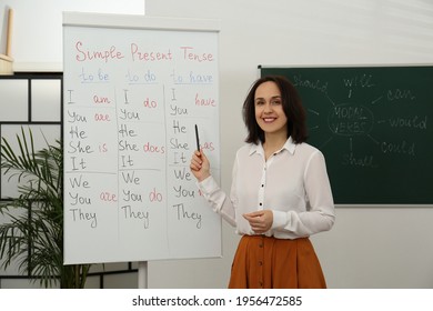 English Teacher Giving Lesson On Simple Present Tense Near Whiteboard In Classroom