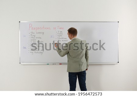 English teacher giving lesson on prepositions of time near whiteboard in classroom, back view