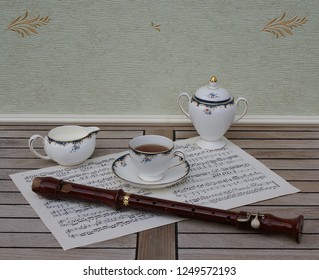 English Teacup With Saucer, Cream Jug And Sugar Bowl, Fine Bone China Porcelain, And A Block Flute On A Sheet Of Music