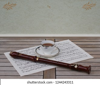 English Teacup With Saucer, Fine Bone China Porcelain, And A Block Flute On A Sheet Of Music